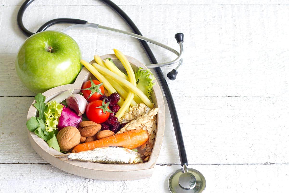 An apple and a bowl of nutritious, healthy food lying on a table next to a stethoscope