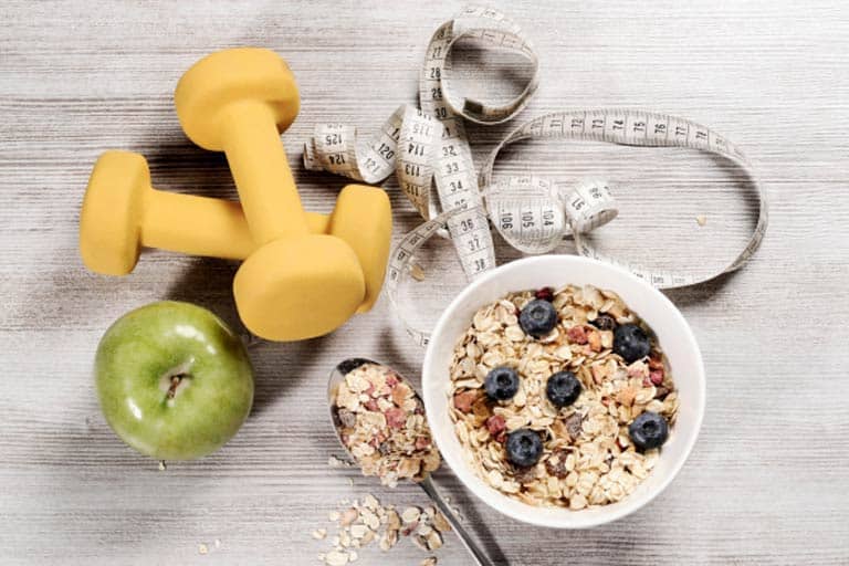 A table with an apple. oatmeal, work out equipment, and other items related to healthy living